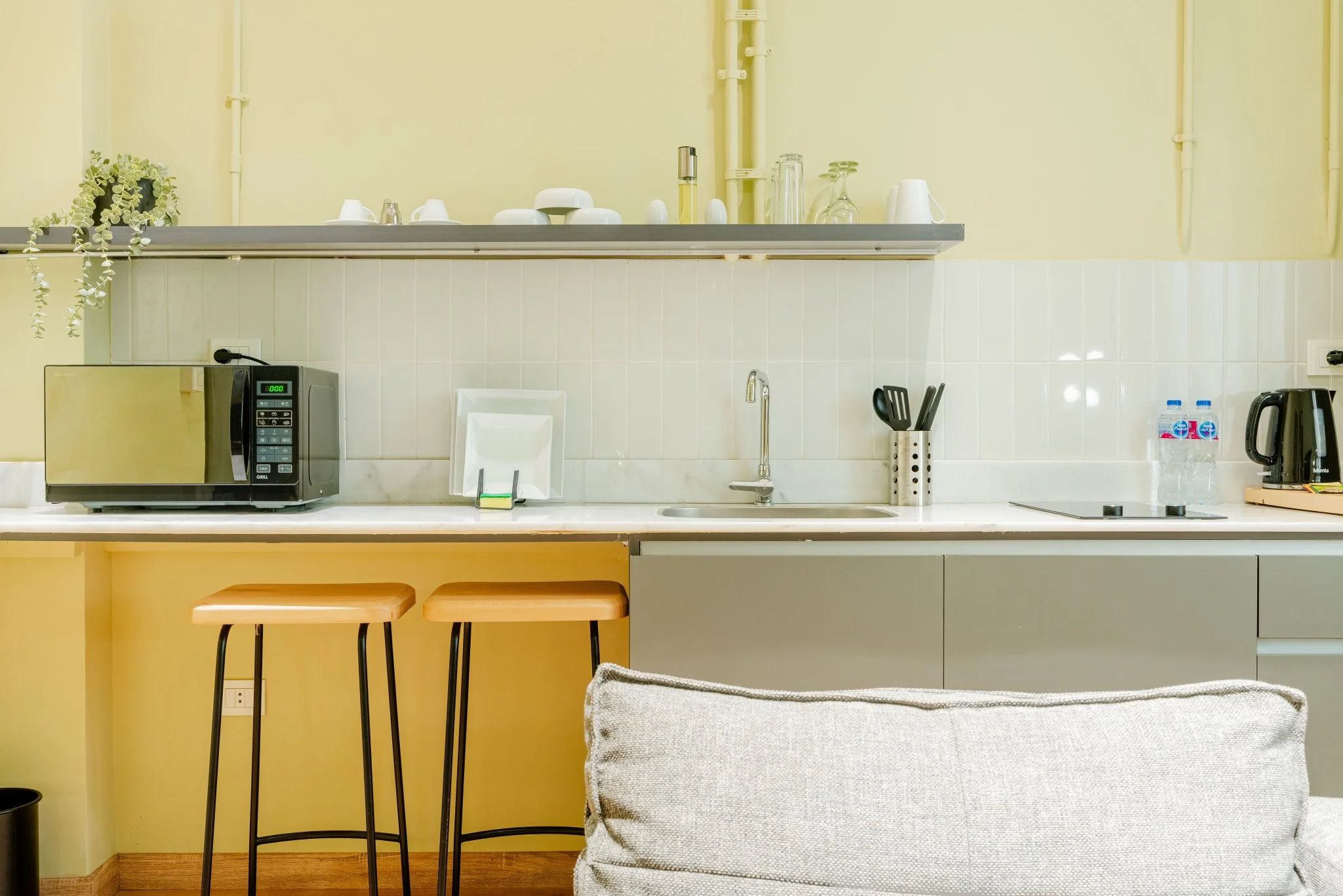 A modern kitchen with a microwave, coffee maker, and bar stools.