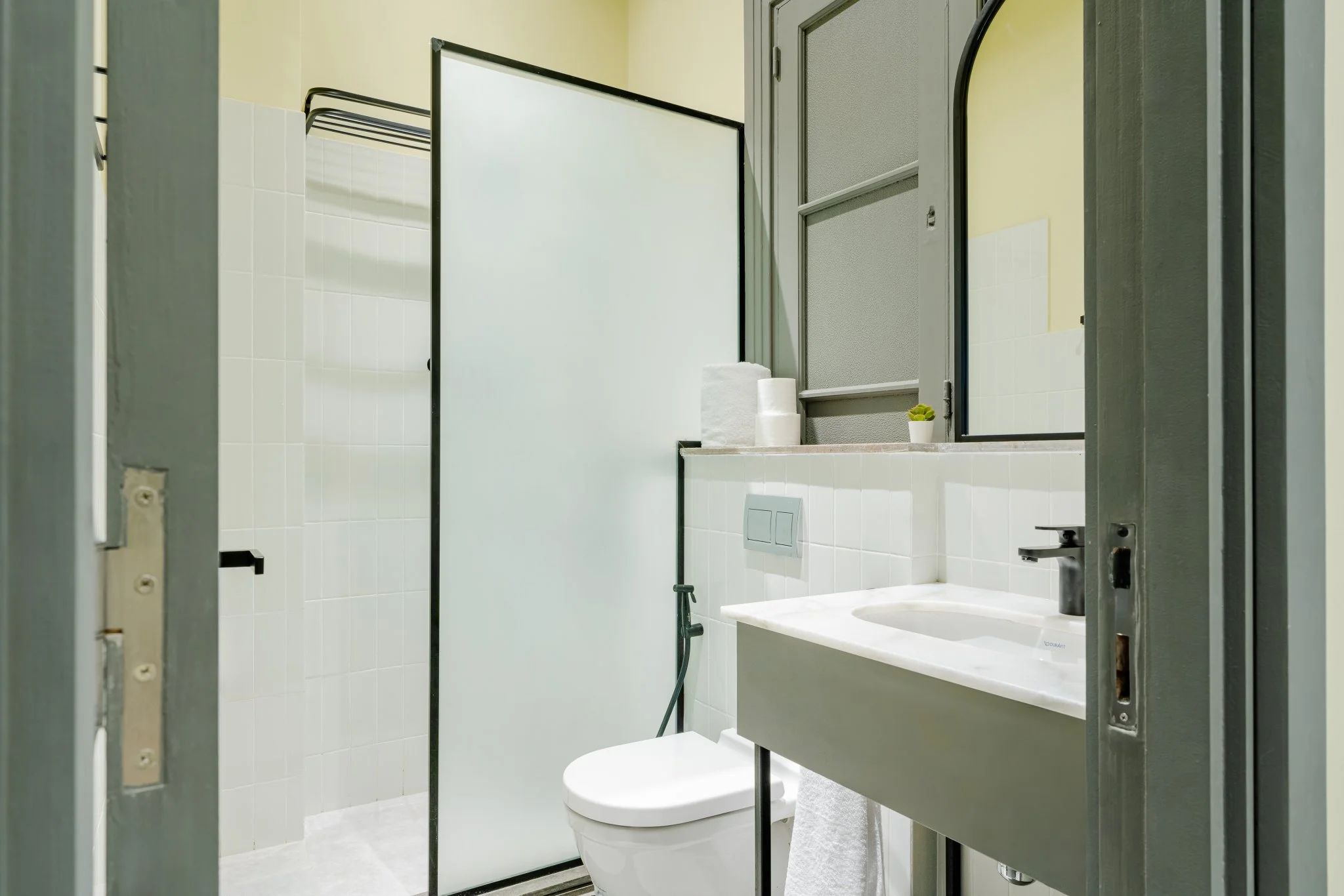 A bathroom with a toilet, a sink, a mirror, and a shower area.