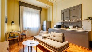 Un espace de vie compact comprenant un canapé, une petite table à manger, un coin cuisine et une fenêtre avec des rideaux.
