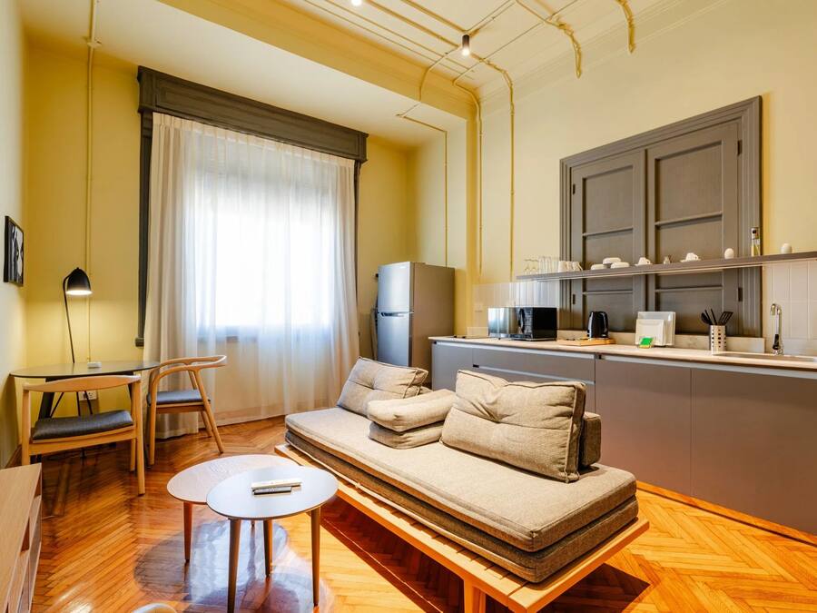 A compact living space with a sofa, a small dining table, a kitchenette, and a window with curtains.