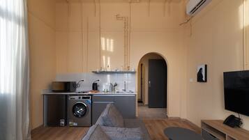 A compact living space with a kitchenette, a washing machine, a sofa, a small table, and a TV.
