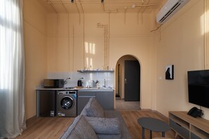 A compact living space with a kitchenette, a washing machine, a sofa, a small table, and a TV. - Studio Apartments Downtown Alexandria Menascehouse (Alexandria)