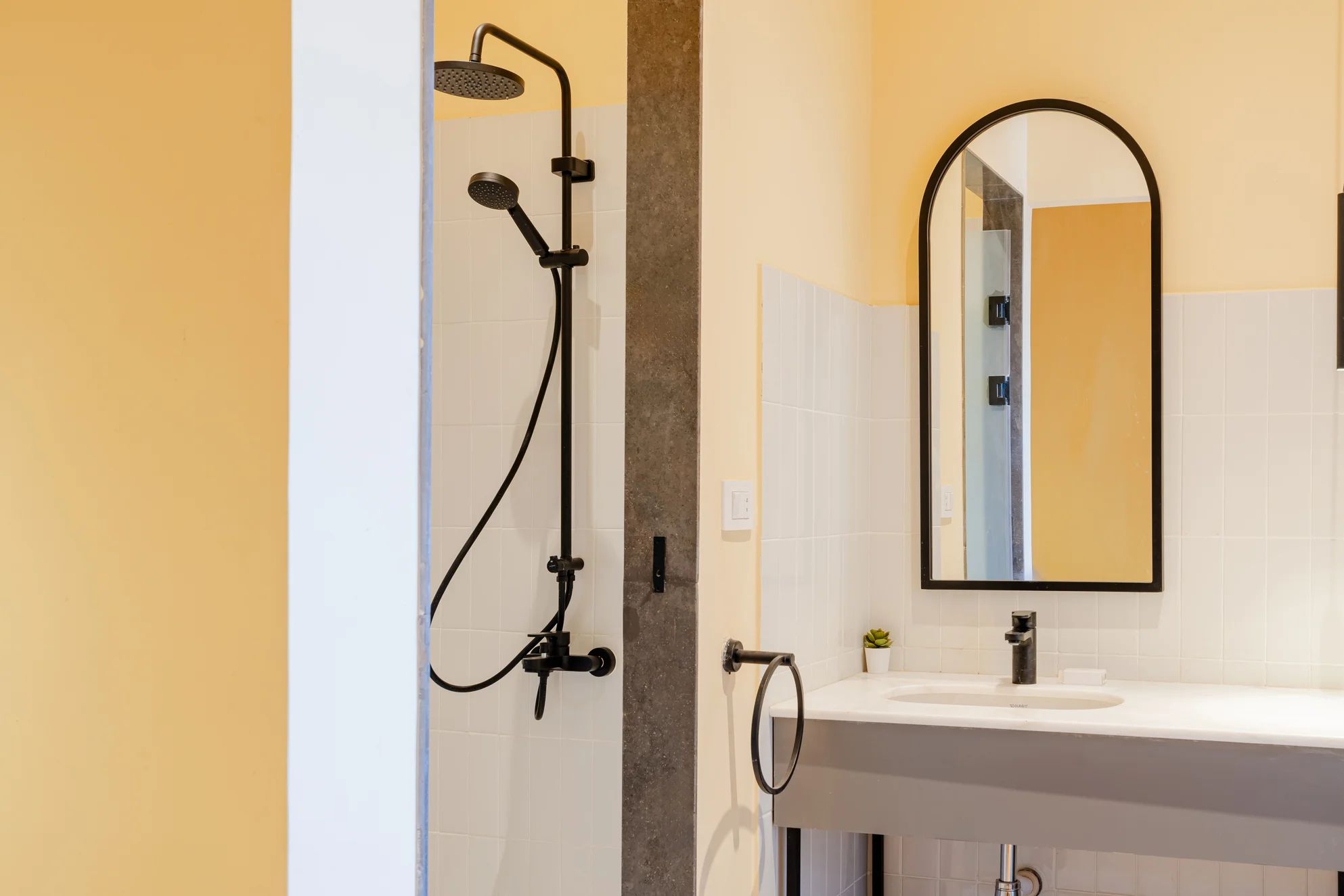 Un baño con ducha, lavamanos, espejo y paredes de azulejos.