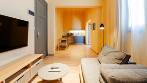 Una sala de estar moderna con un televisor de pantalla plana, un sofá, una mesita de centro y una cocina al fondo.
