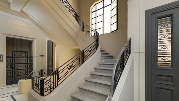 Una escalera de mármol con barandillas negras y una puerta oscura con paneles de vidrio ornamental.