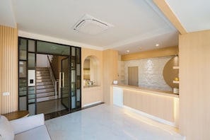 A modern reception area with a glass door entrance, a staircase, and a reception desk with a stone accent wall. - Vera Residecnes (Mae Sai)