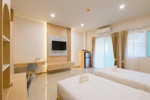 A hotel room with two beds, a TV mounted on the wall, a desk with a chair, a refrigerator, and an air conditioning unit. - Vera Residecnes (Mae Sai)