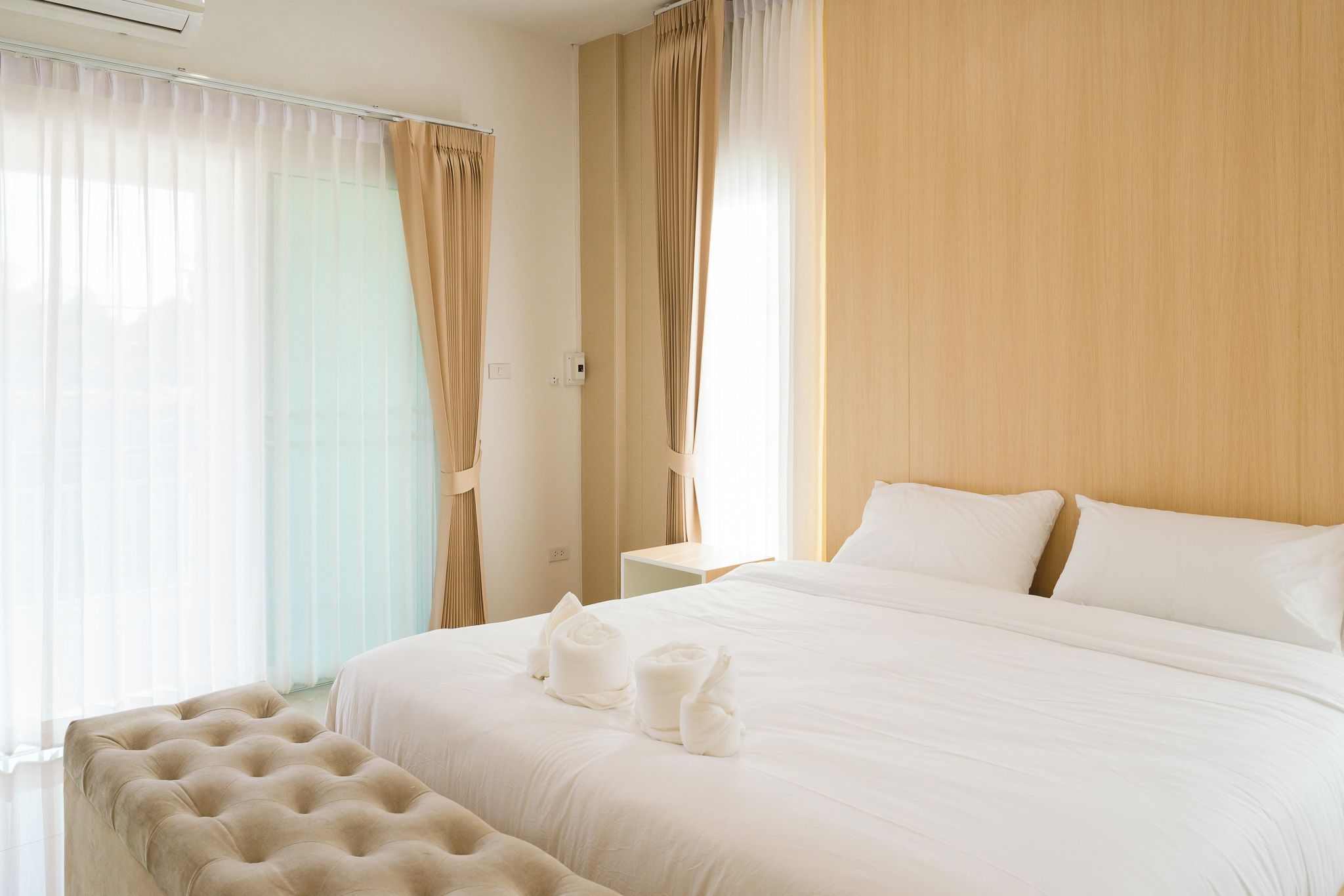 A hotel room with a large bed, two pillows, a bedside table, and a window with curtains.