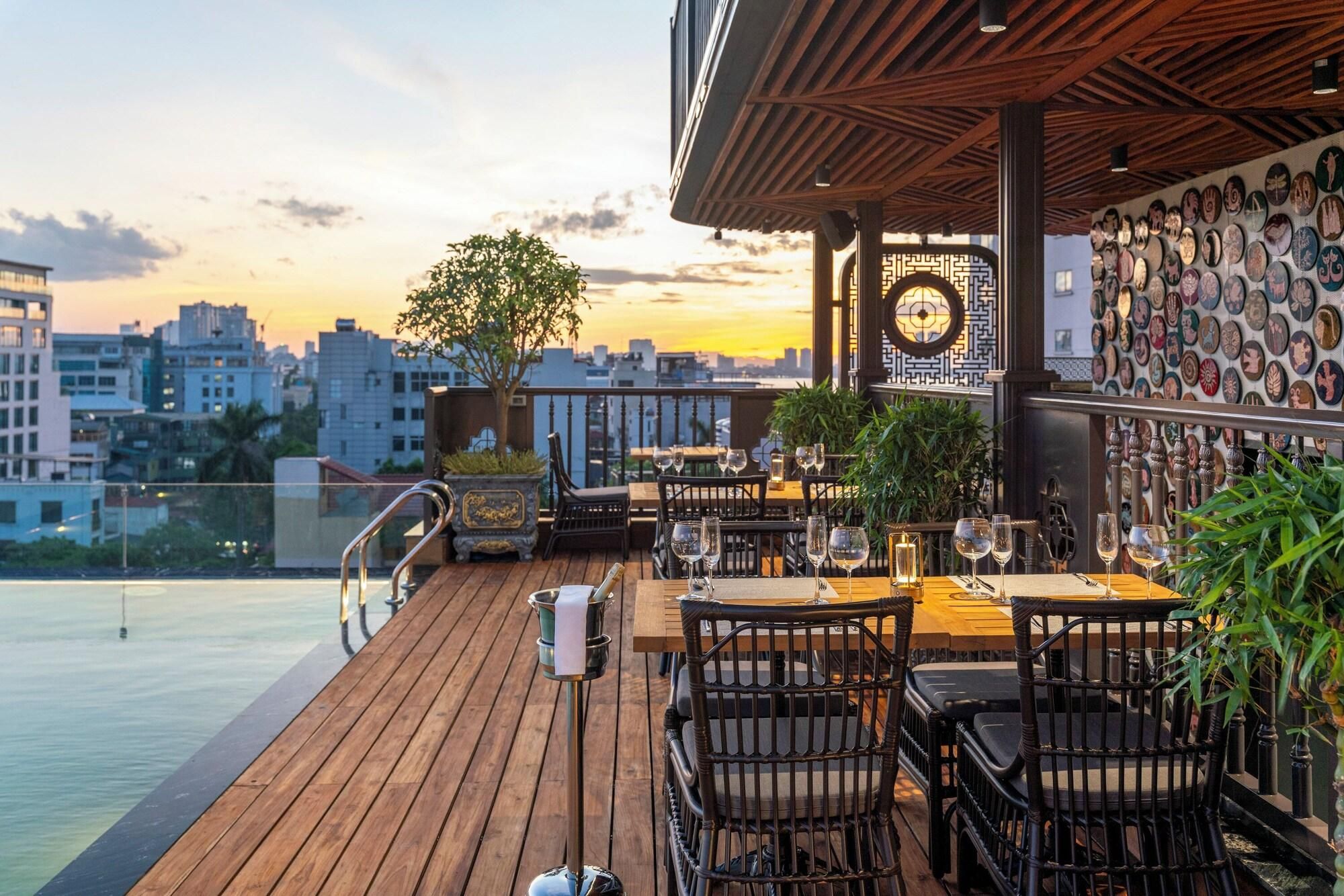 Um bar no terraço com soalho de madeira, mesas, cadeiras e vista para a cidade ao pôr do sol.