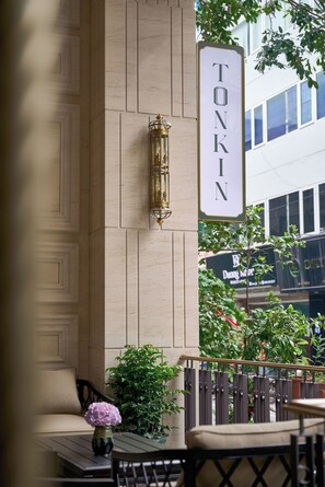 A cafe with a sign reading "TONKIN" and outdoor seating with a table, chair, and a vase with flowers. - Tonkin Luxury Boutique Hotel & Spa (Hanoi)