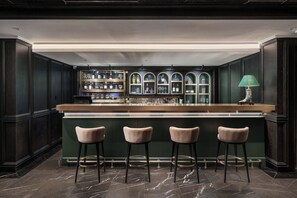 A bar area with a counter, three cushioned bar stools, and shelves with bottles and glasses. - Tonkin Luxury Boutique Hotel & Spa (Hanoi)