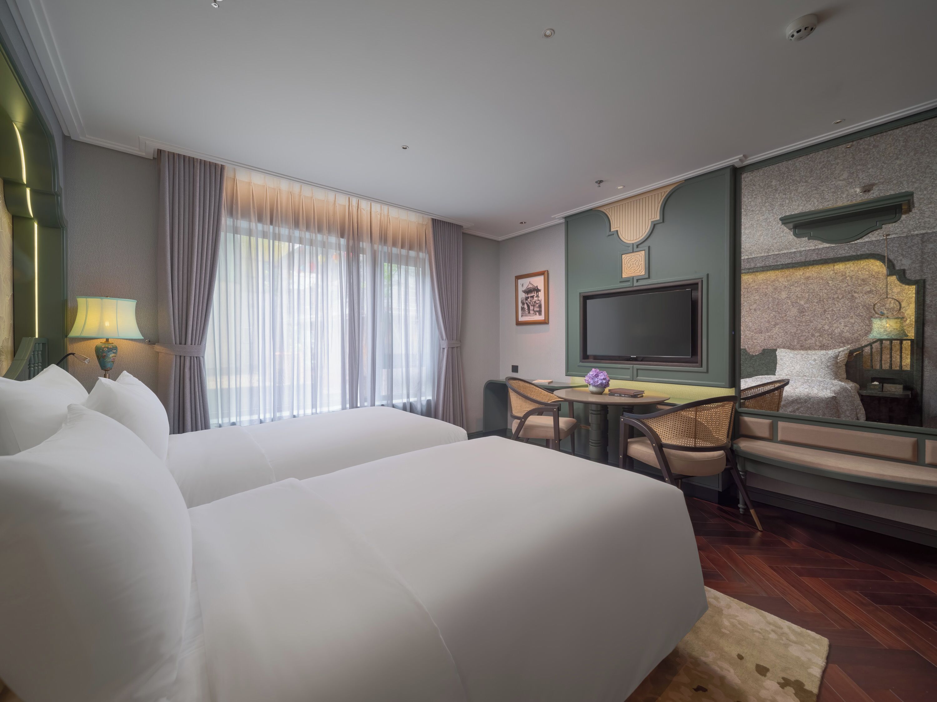 Ett hotellrum med två sängar, ett skrivbord med stolar, en TV och ett stort fönster med gardiner.