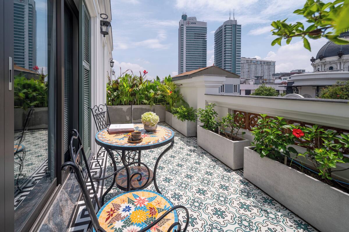A balcony with a tiled floor, a table with a vase of flowers, and potted plants.