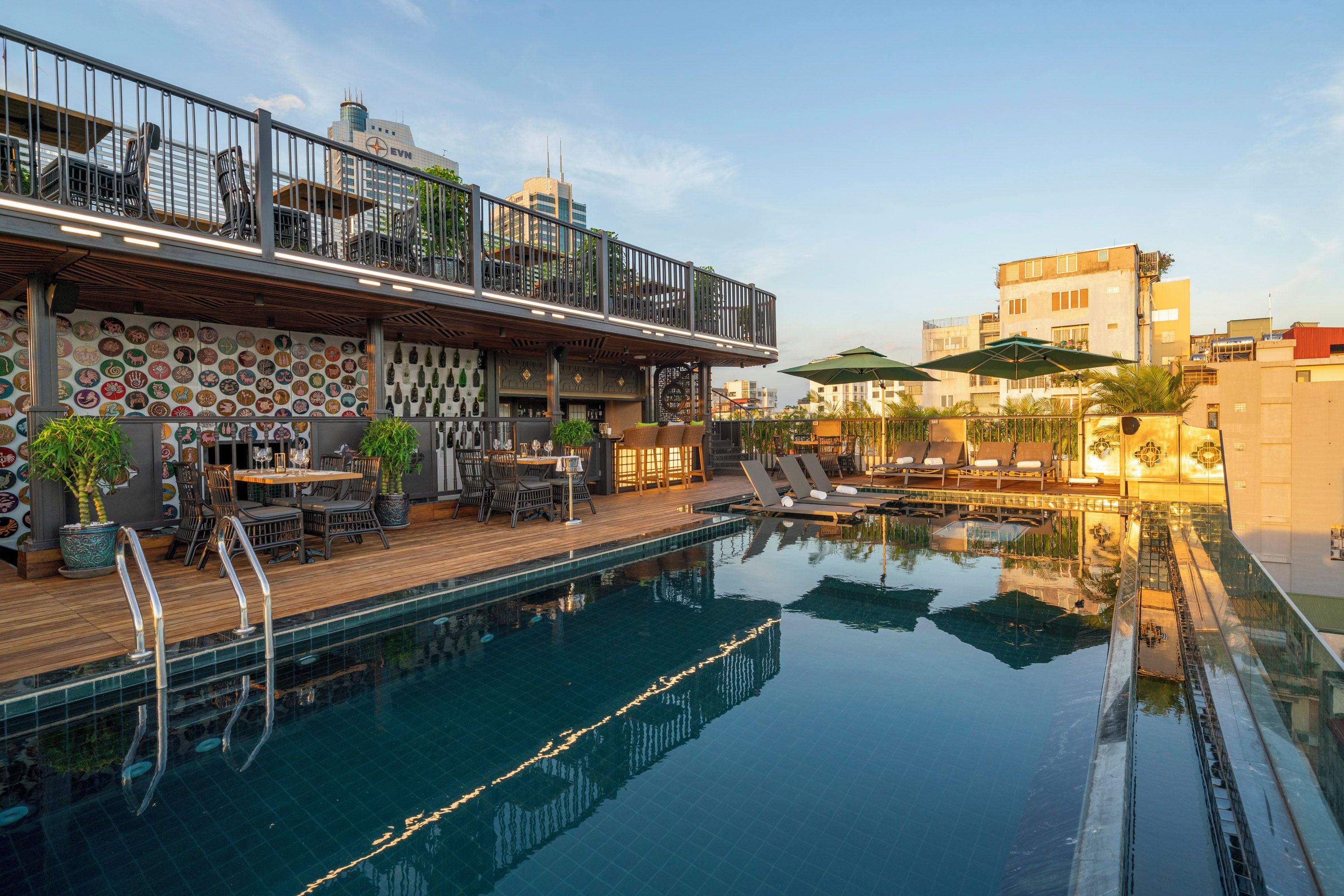 A rooftop pool with lounge chairs, a bar area with chairs and tables, and a view of the city skyline.