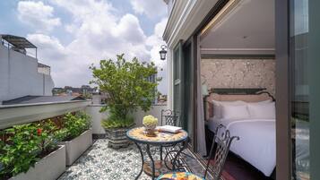 A balcony with a bed, a table, and chairs. There is a tree and a potted plant on the balcony.