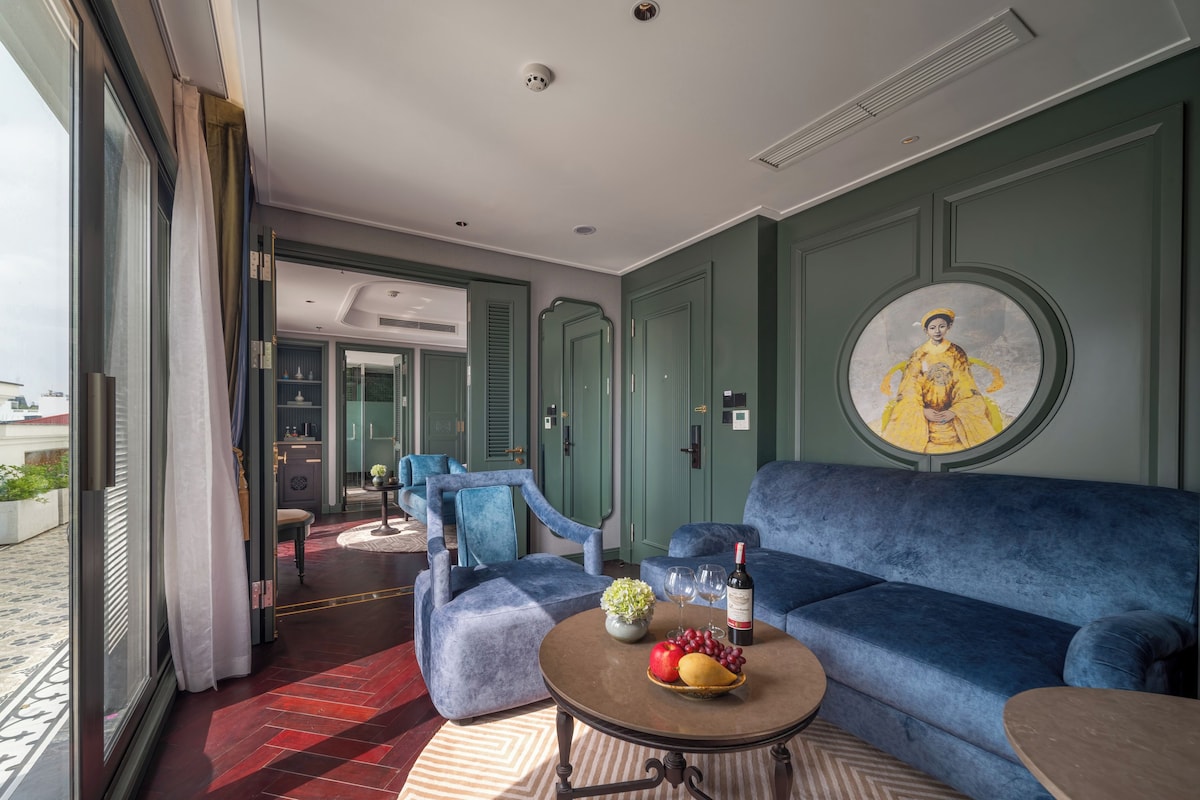 A modern living room with a blue sofa, a round coffee table with fruit and wine, and a large painting on the wall.