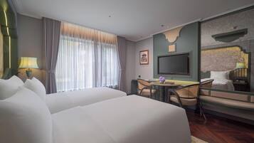 A hotel room with two large beds, a desk with chairs, a television, and a large mirror.