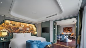Una habitación de hotel con una cama grande, un sillón azul, una mesita redonda y un mural decorativo en la pared.