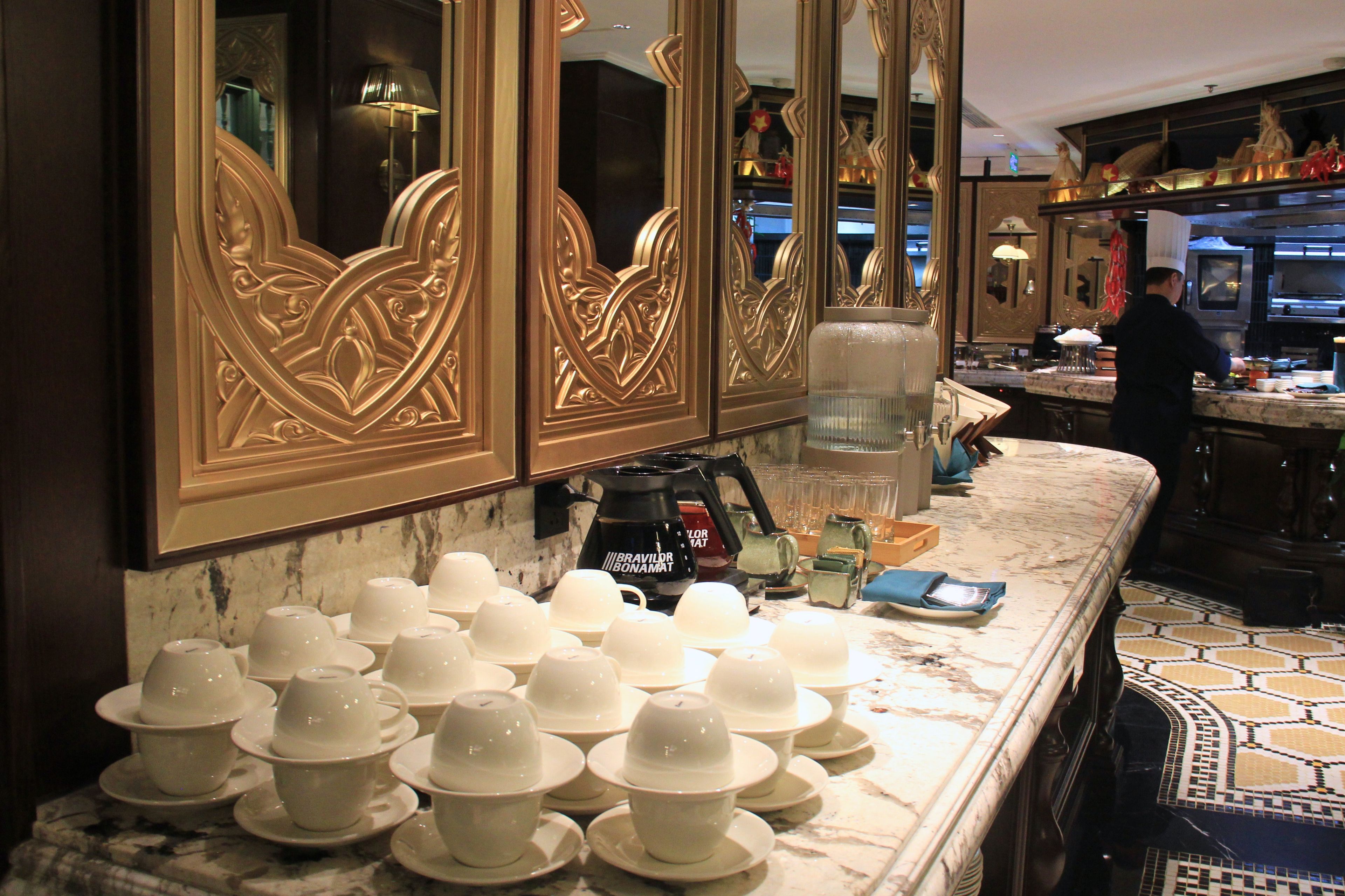A hotel kitchen with a marble countertop, a coffee machine, and a chef preparing food.