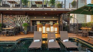 A rooftop bar with a pool, lounge chairs, and a bar area with a wine display.