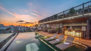 A rooftop infinity pool with lounge chairs and a bar area.