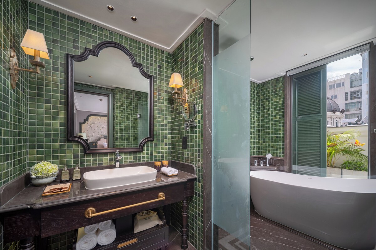 A modern bathroom with green mosaic tiles, a large mirror, a vanity with a sink, and a bathtub.