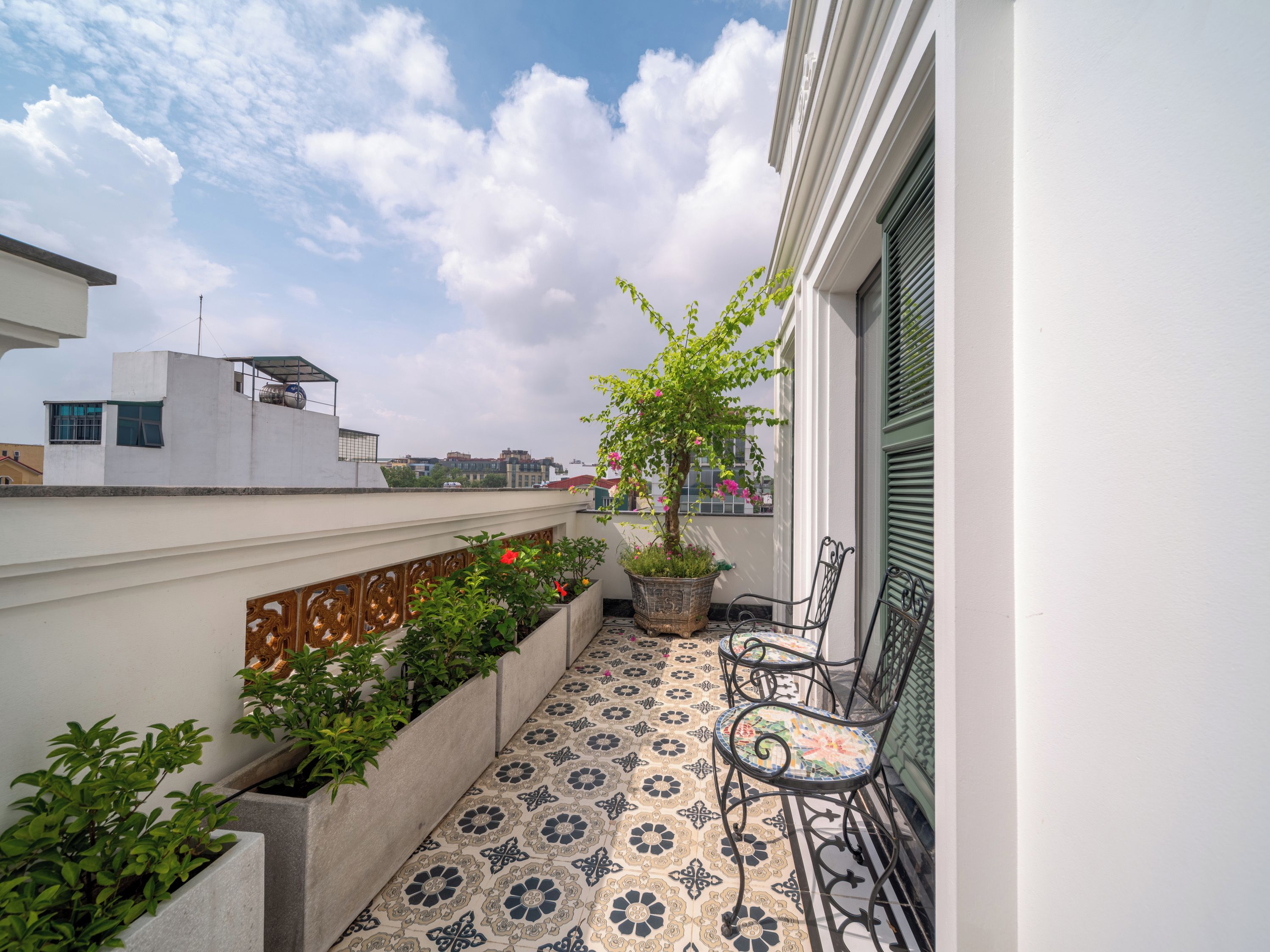 A balcony with patterned flooring, potted plants, and two chairs.