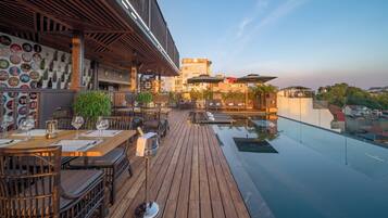 A rooftop bar with wooden flooring, outdoor seating, and a pool.