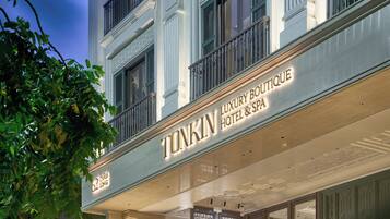 El exterior del Hotel Boutique Tonkin Luxury & Spa, con un letrero y un árbol en primer plano.