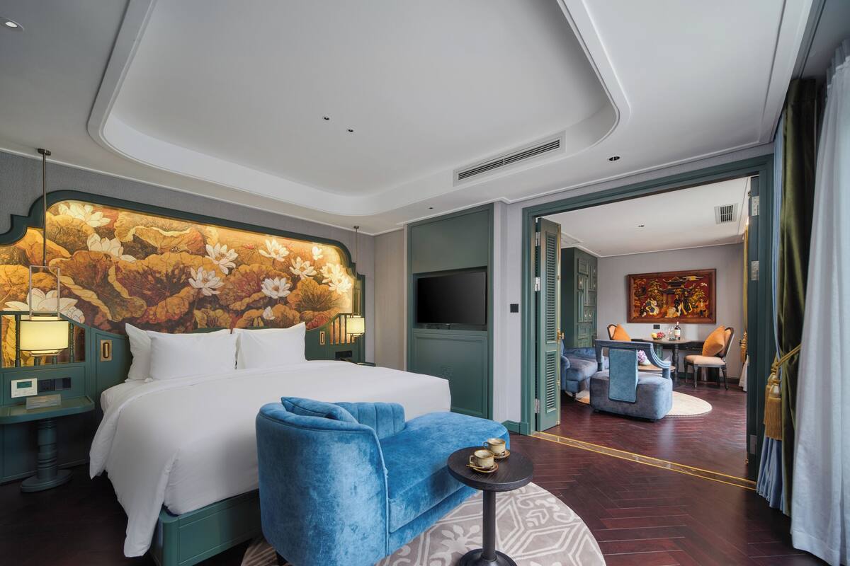 A hotel room with a large bed, a blue armchair, a round table, and a decorative headboard.