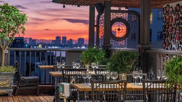 An outdoor dining area with tables and chairs, a city skyline view, and decorative wall art.