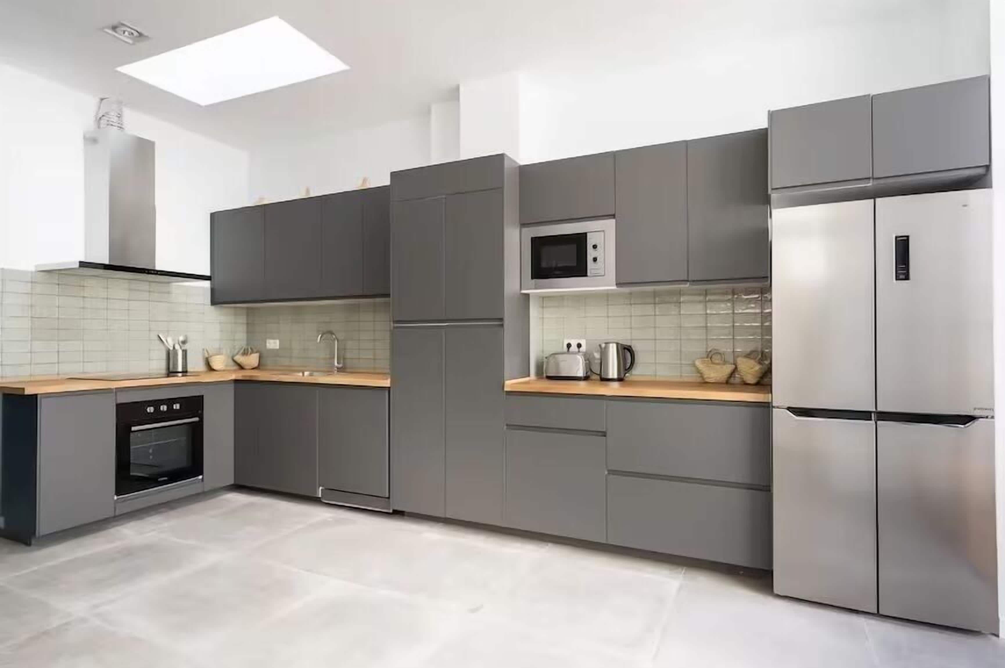 A modern kitchen with grey cabinets, a stainless steel refrigerator, a microwave, and a built-in oven.