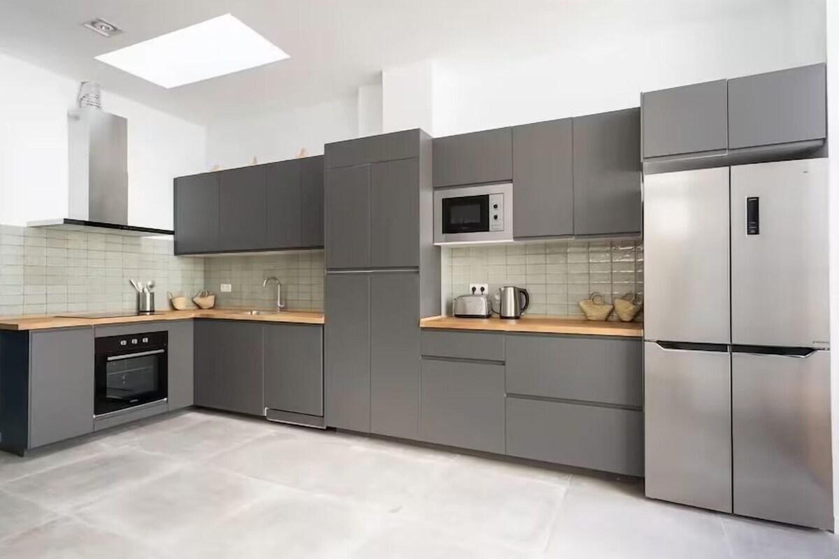 A modern kitchen with grey cabinets, a stainless steel refrigerator, a microwave, and a built-in oven.