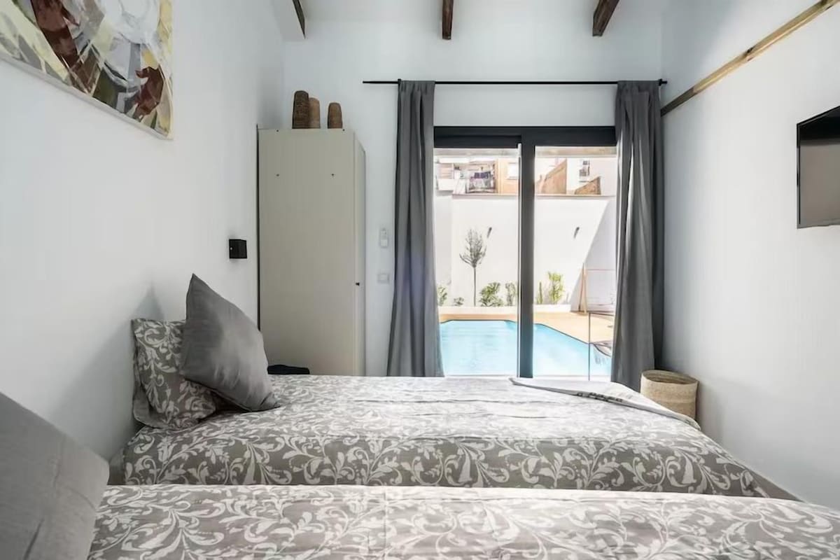 A bedroom with a bed, a wardrobe, and a view of a swimming pool through a glass door.