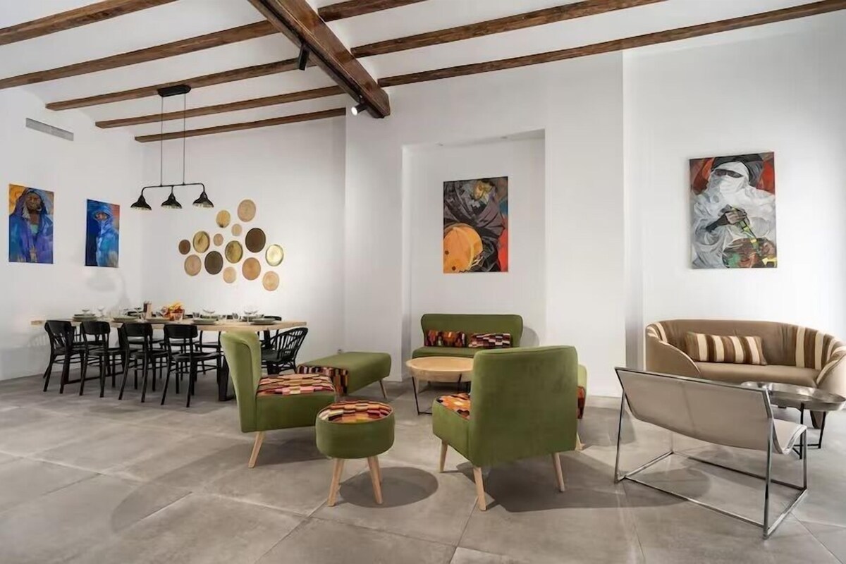 A modern interior with a dining area, green armchairs, a sofa, and artwork on the walls.