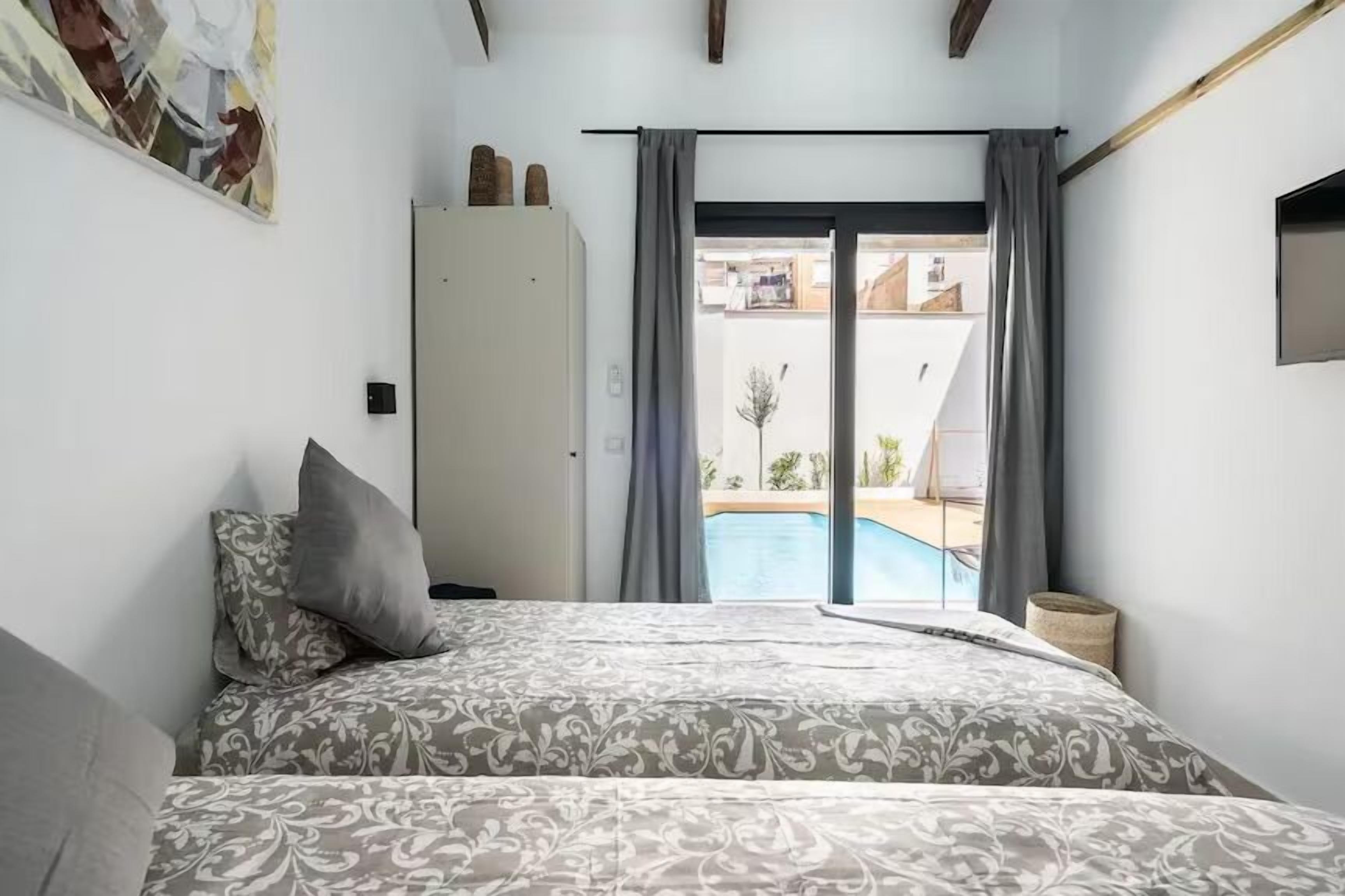 A bedroom with a bed, a wardrobe, and a view of a swimming pool through a glass door.