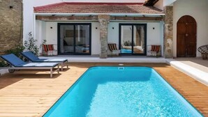 A modern pool area with a wooden deck, two lounge chairs, and a clear blue pool. - Villa Ramon (Valencia)