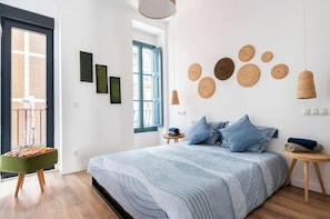 A bedroom with a bed, a small stool, a window, and wall art. - Villa Ramon (Valencia)