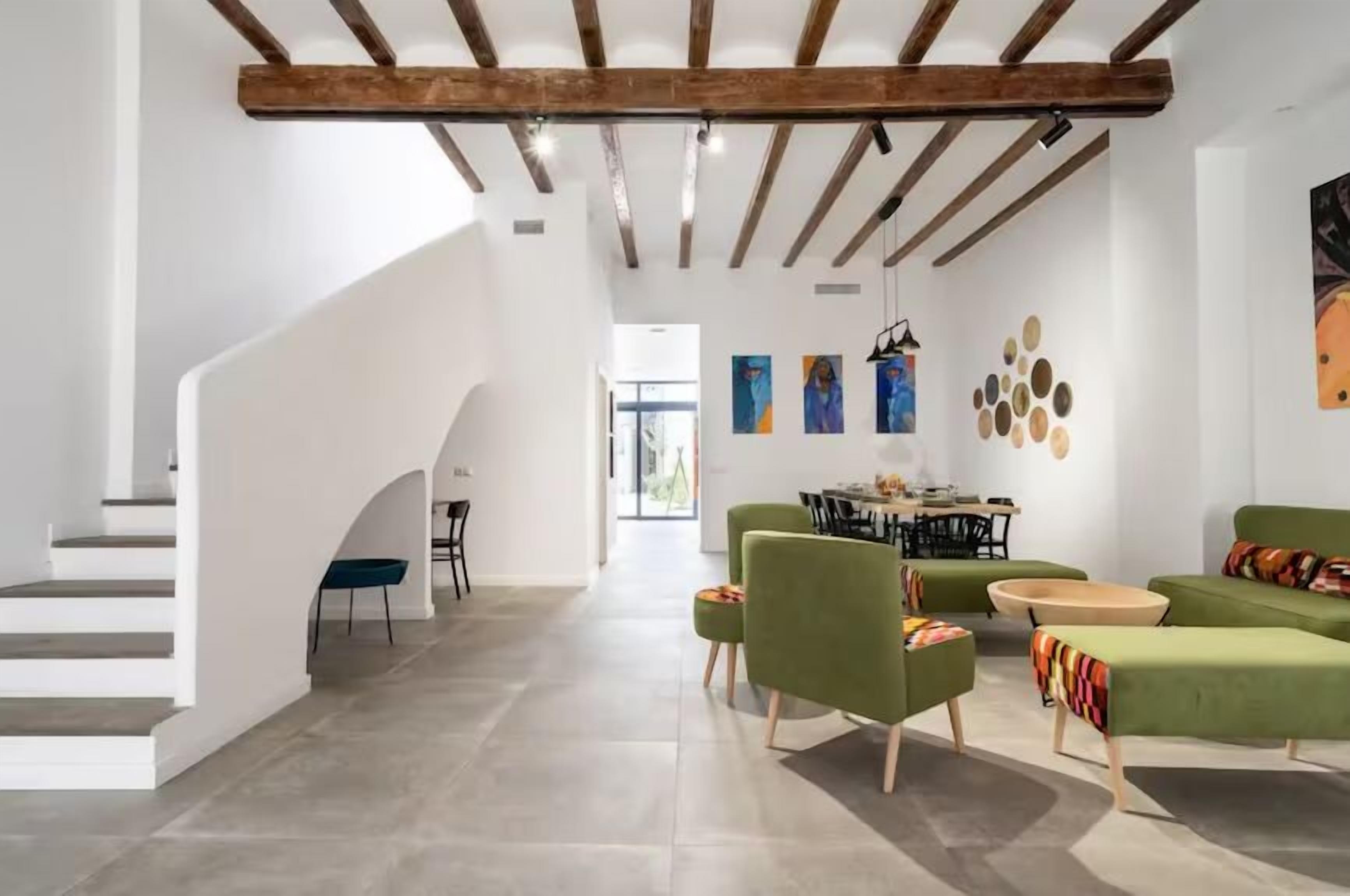 Uma sala de estar espaçosa com escada, sofás verdes, mesa de jantar e obras de arte nas paredes.