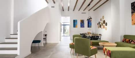 A spacious living area with a staircase, green sofas, a dining table, and artwork on the walls.