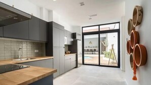 A modern kitchen with grey cabinets, a wooden countertop, and a large window overlooking a pool area. - Villa Ramon (Valencia)