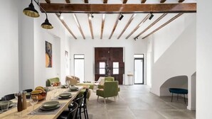A spacious dining area with a long wooden table set for a meal, surrounded by chairs. There are two pendant lights above the table, and the room has exposed wooden beams on the ceiling. - Villa Ramon (Valencia)