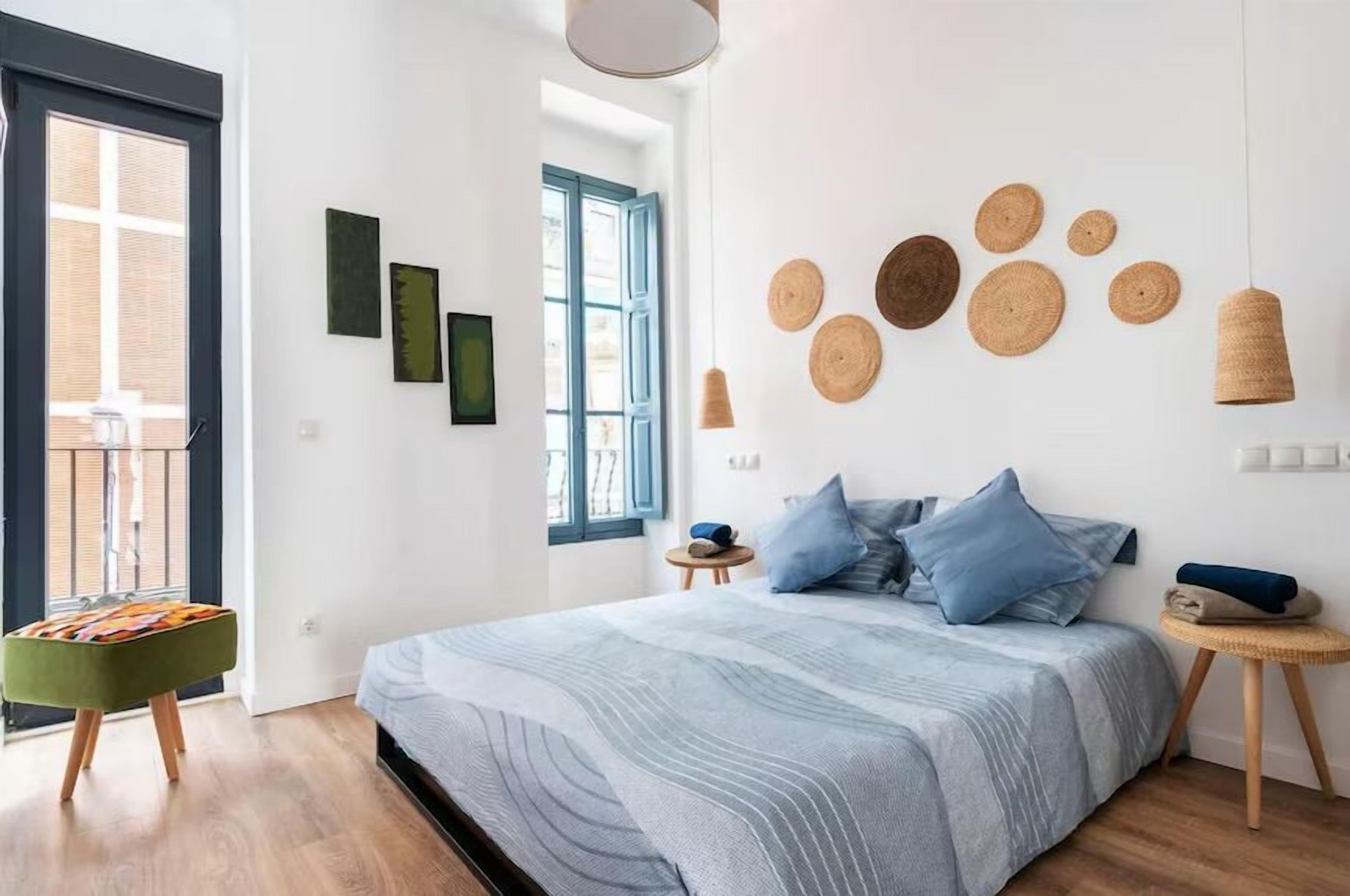 Un dormitorio con cama, un taburete pequeño, una ventana y decoración en la pared.