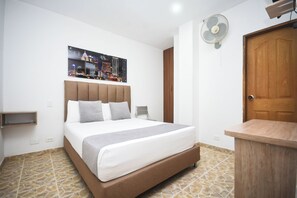 Ein Hotelzimmer mit einem Bett, einem Wandventilator, einer Holztür und einem gefliesten Boden.