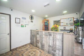 Ein Empfangsbereich mit Holztresen, einer Uhr, einem Kühlschrank und einem Schwarzesbrett mit Aushängen.