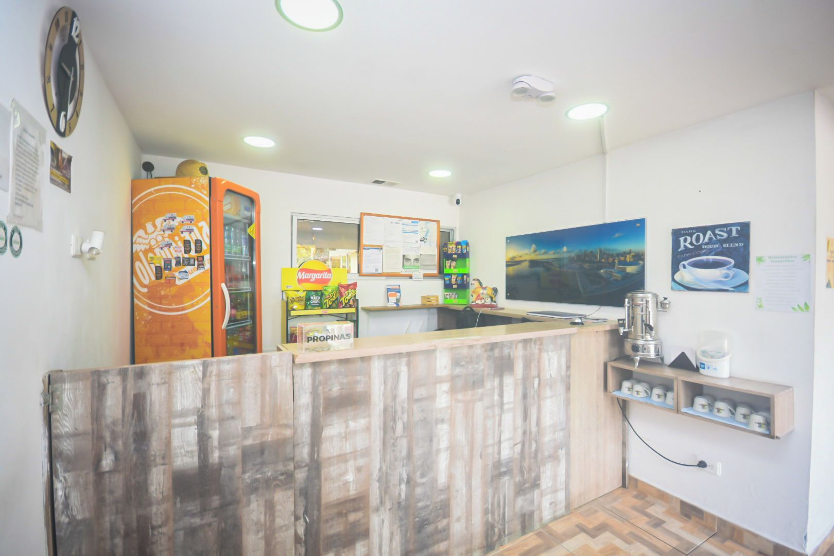 A reception area with a wooden counter, a refrigerator, a coffee machine, and a wall-mounted TV.