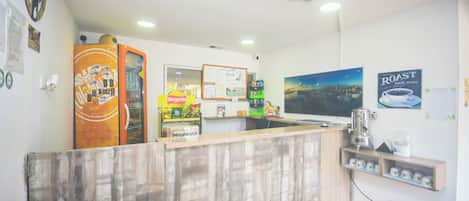 A reception area with a wooden counter, a refrigerator, a coffee machine, and a wall-mounted TV.