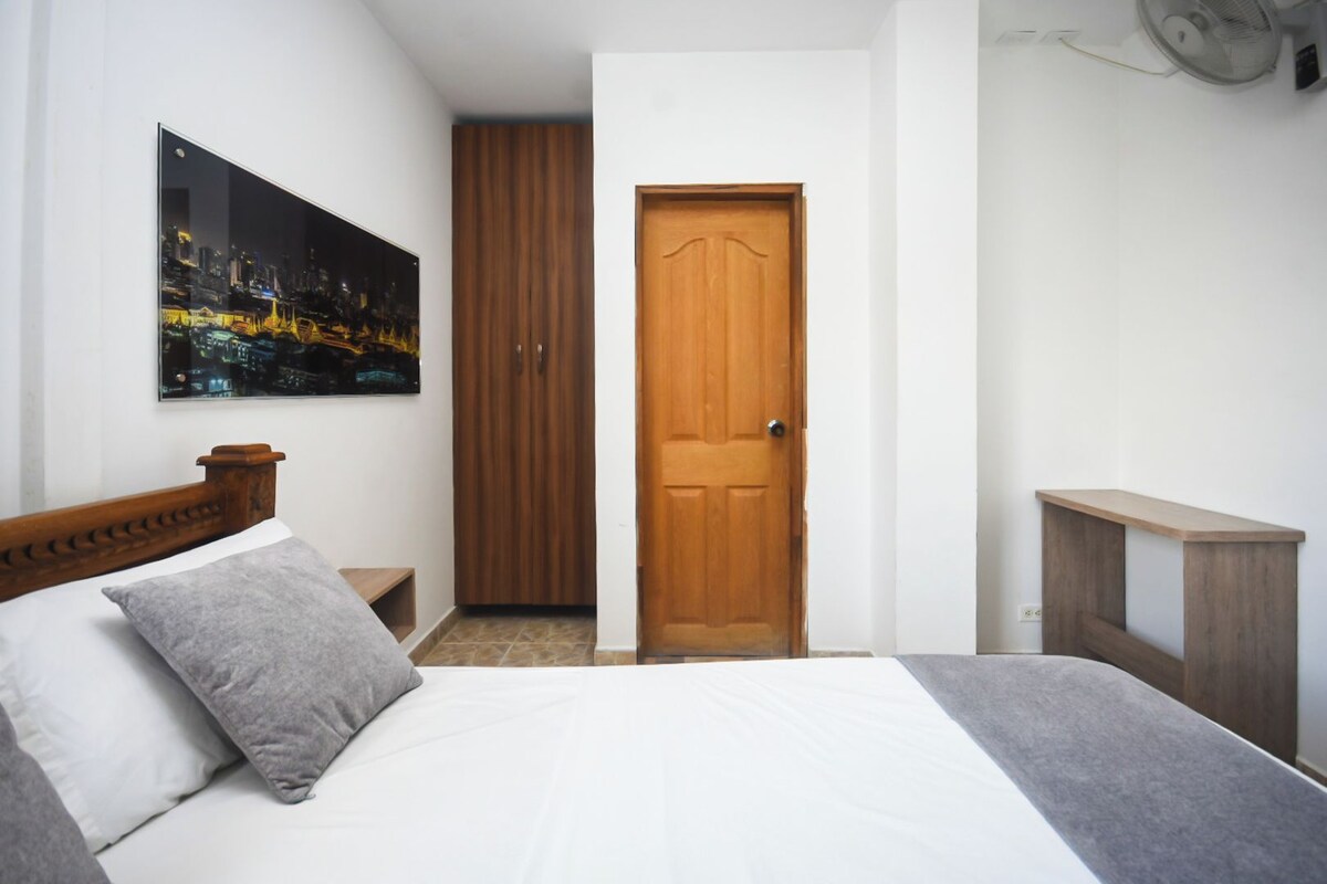 Ein Schlafzimmer mit Bett, einer Holztür, einem Stadtbildgemälde bei Nacht und einem kleinen Holztisch.