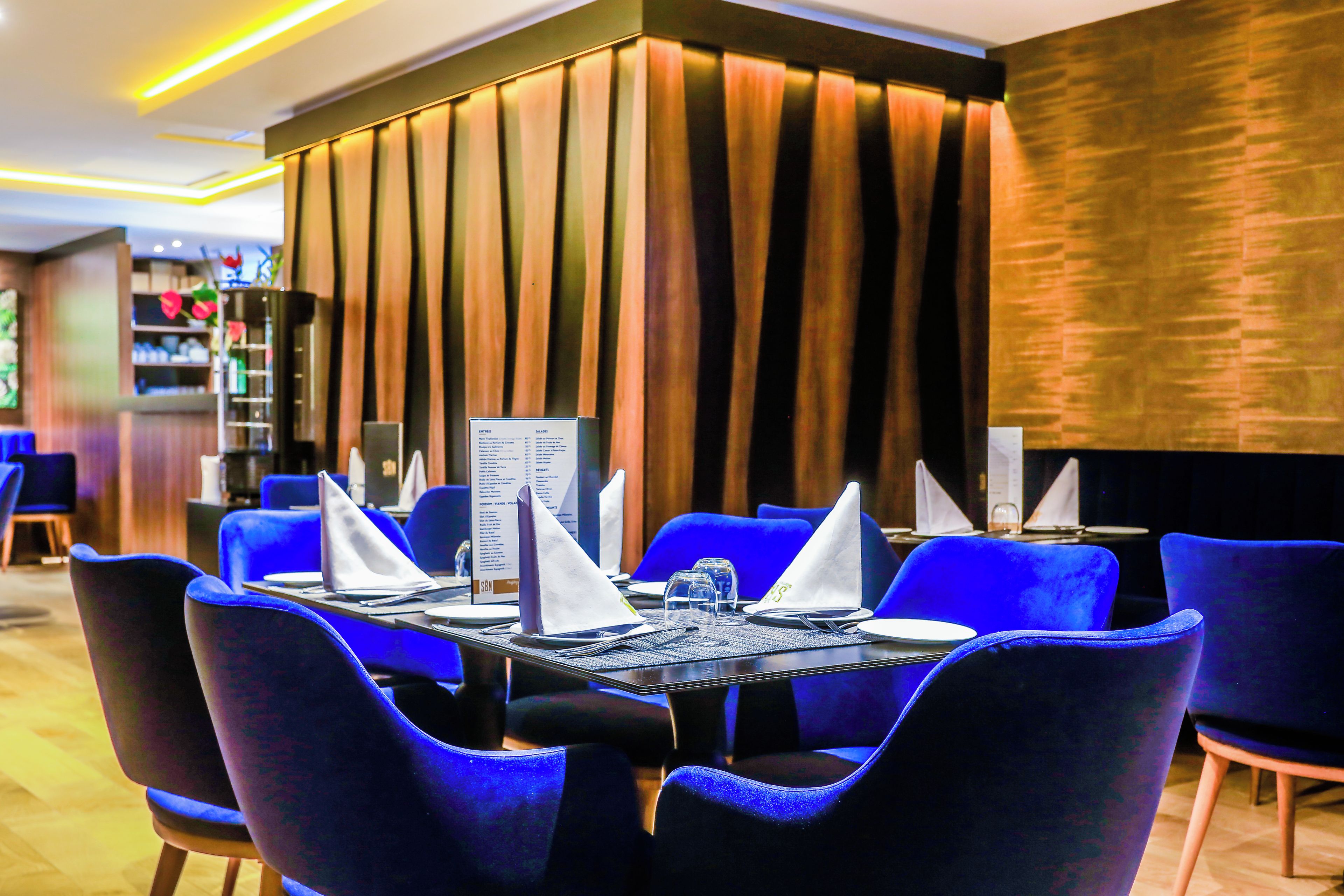 A restaurant with blue chairs, a black table, and a menu stand.