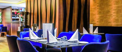 A restaurant with blue chairs, a black table, and a menu stand.